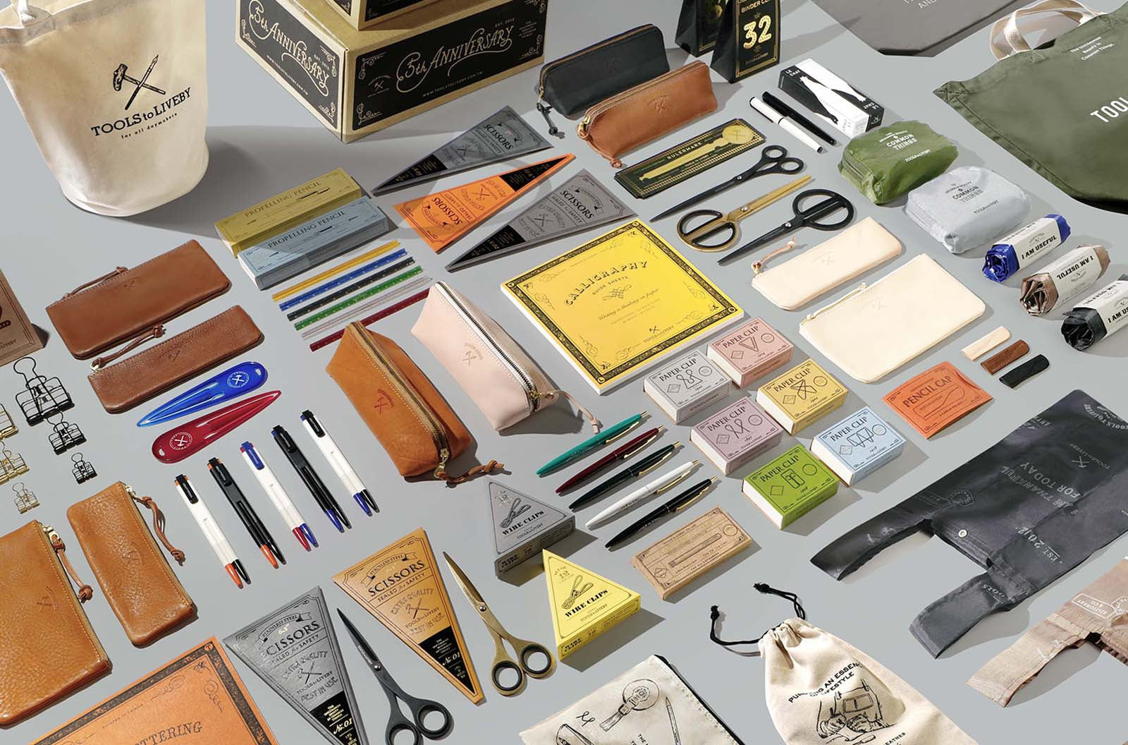 Overhead flat-lay of the TOOLS to LIVEBY collection, showcasing premium analog stationery, Japanese steel scissors, leather pen cases, brass clips, and lifestyle gear.