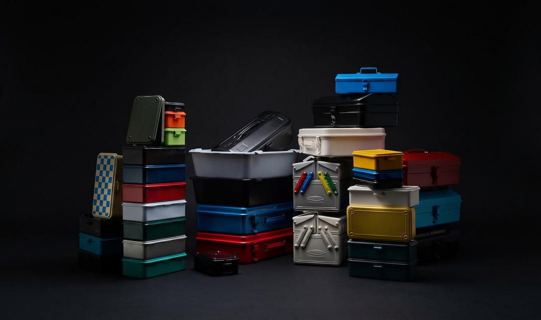 Stack of Japanese Toyo Steel toolboxes and storage trunks in assorted colors against a dark background.