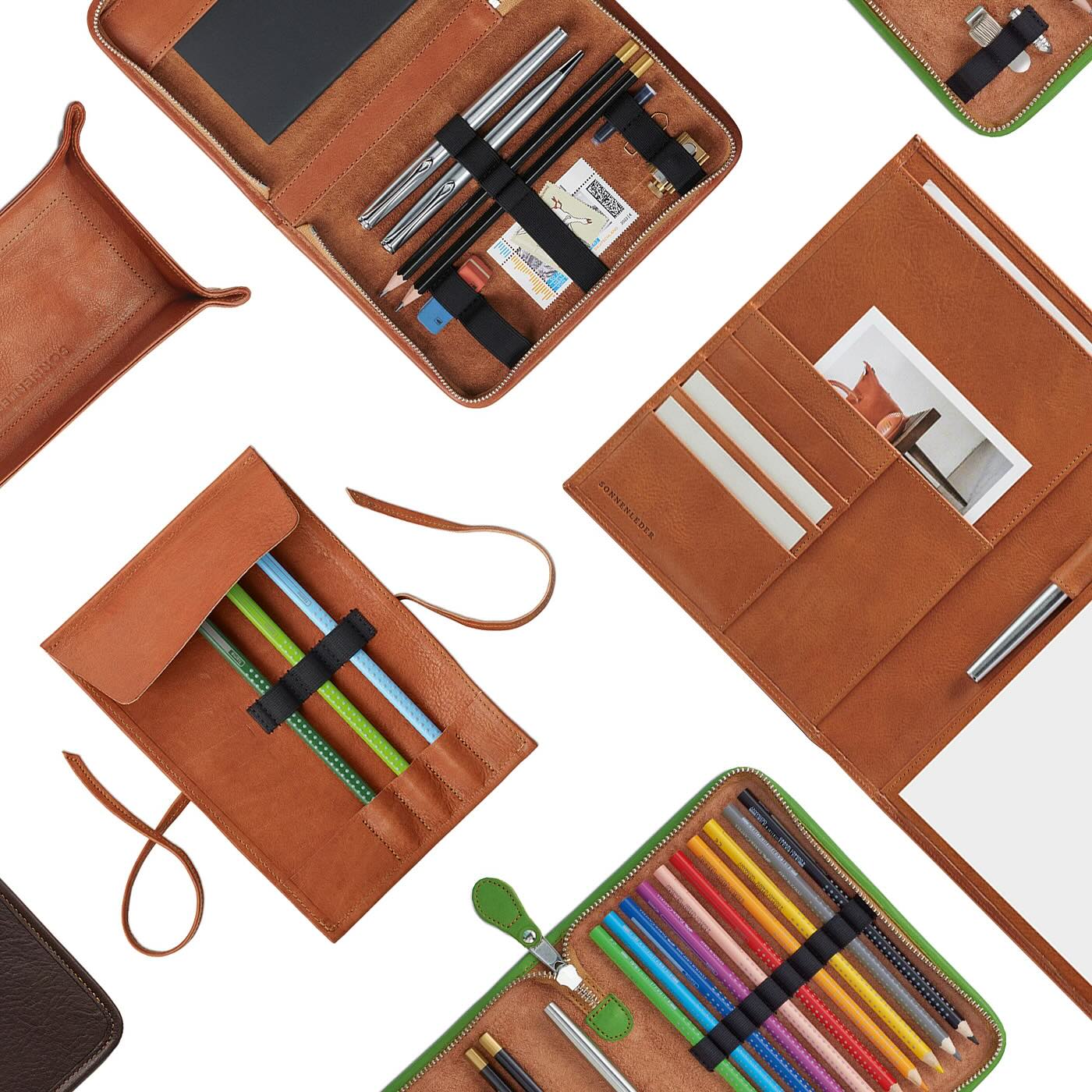 An overhead flat-lay of the Sonnenleder collection in Natural leather, featuring various pen cases, a leather pen wrap, and a desk tray, all organized with fountain pens and pencils to showcase the rich texture and versatile storage of German vegetable-tanned leather.