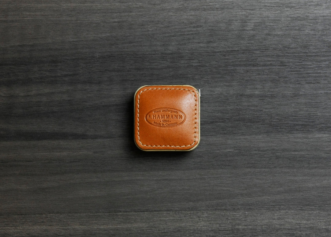 Top-down photograph of the F. Hammann 5205 Coxorange Alpina Leather Tape Measure resting on dark wood grain.