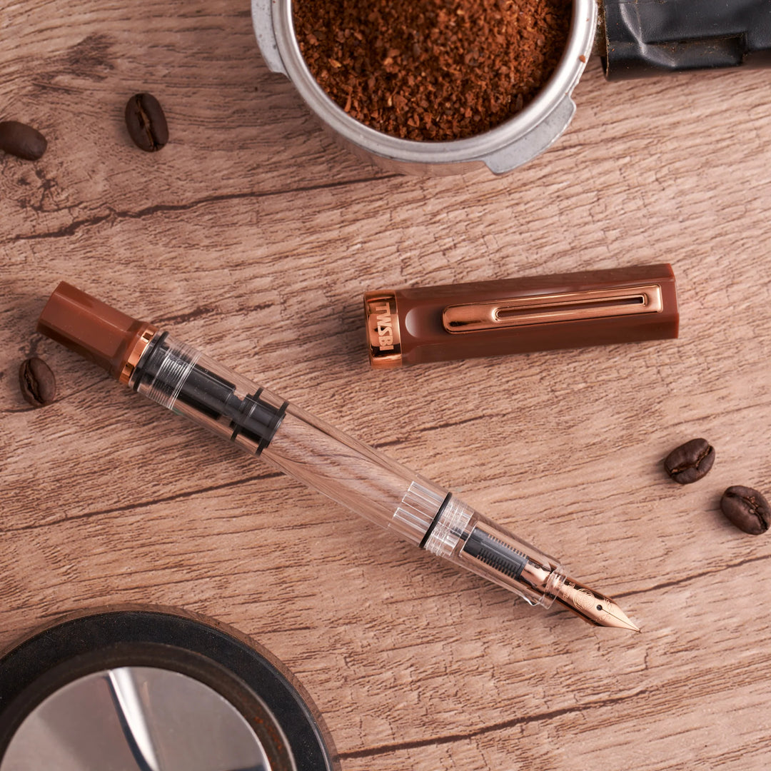 TWSBI ECO Fountain Pen – Espresso Bronze on a wooden surface with coffee beans and a container of ground coffee.