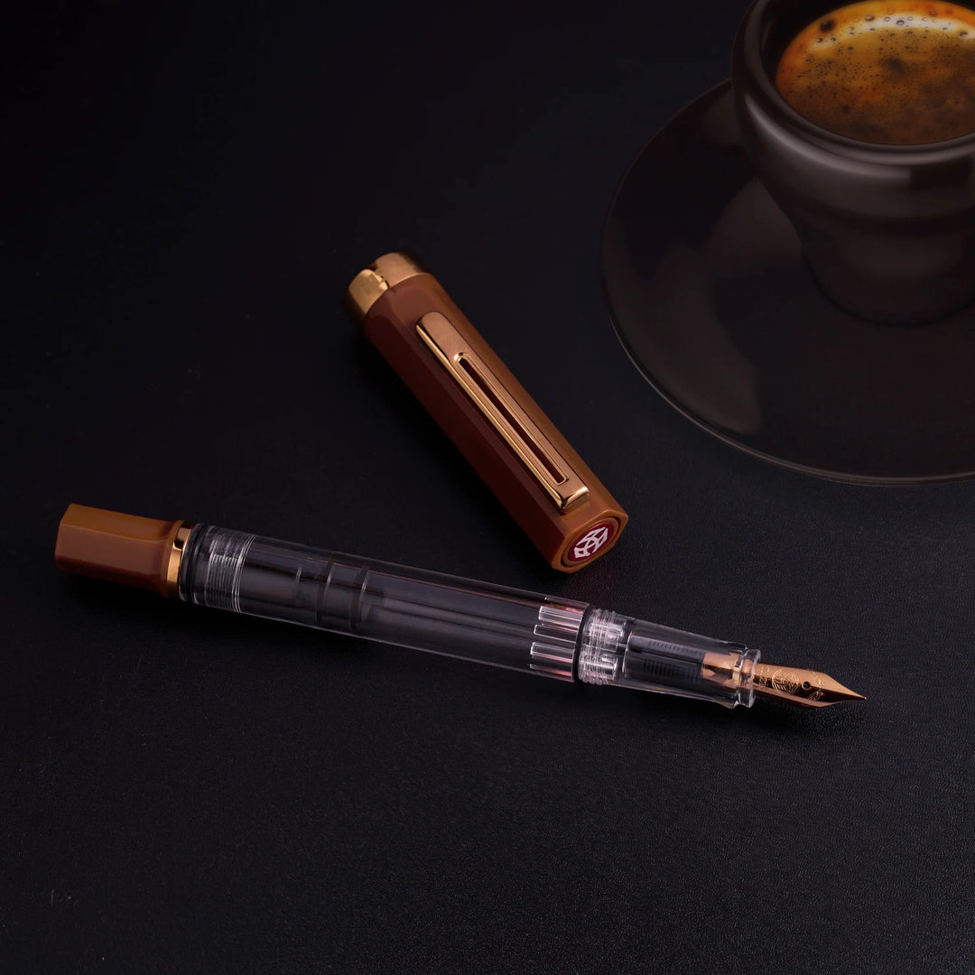 TWSBI ECO Fountain Pen – Espresso Bronze on a dark surface with a cup of coffee in the background