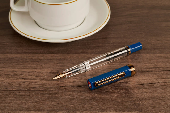 TWSBI ECO Fountain Pen – Indigo Blue Bronze on a wooden surface next to a white cup and saucer.