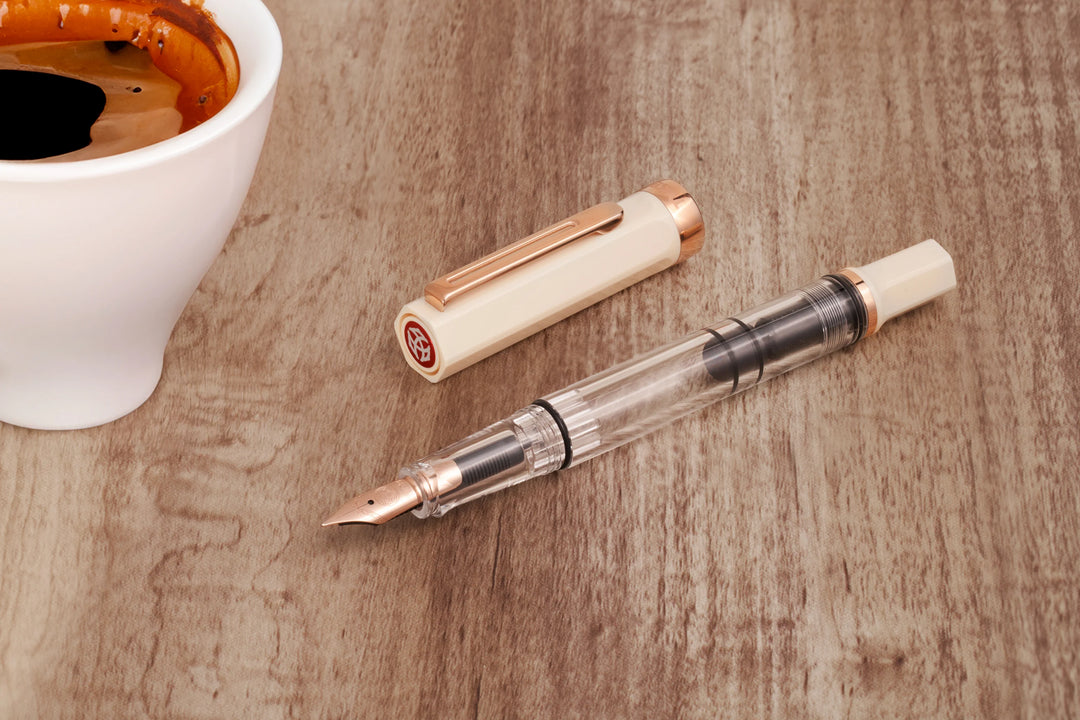 TWSBI ECO Fountain Pen – Creme Rose Gold on a wooden surface with a cup of coffee.