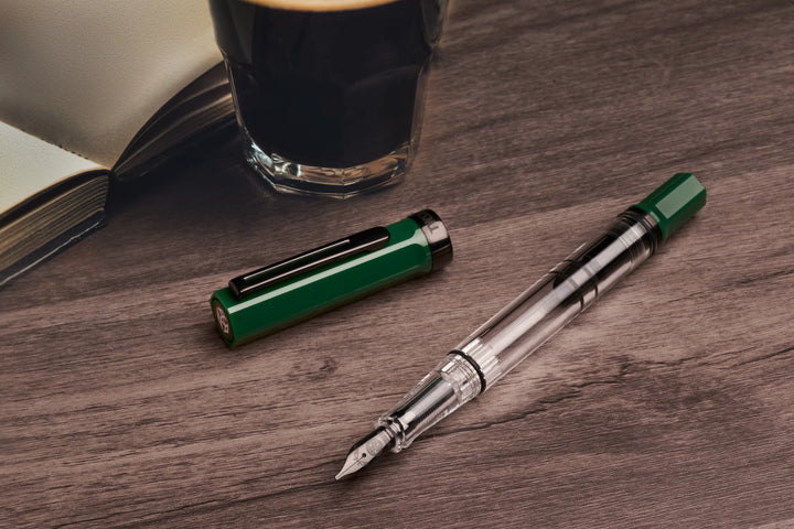 TWSBI ECO Fountain Pen – Irish Green Onyx on a wooden surface with a glass of black coffee and an open book.