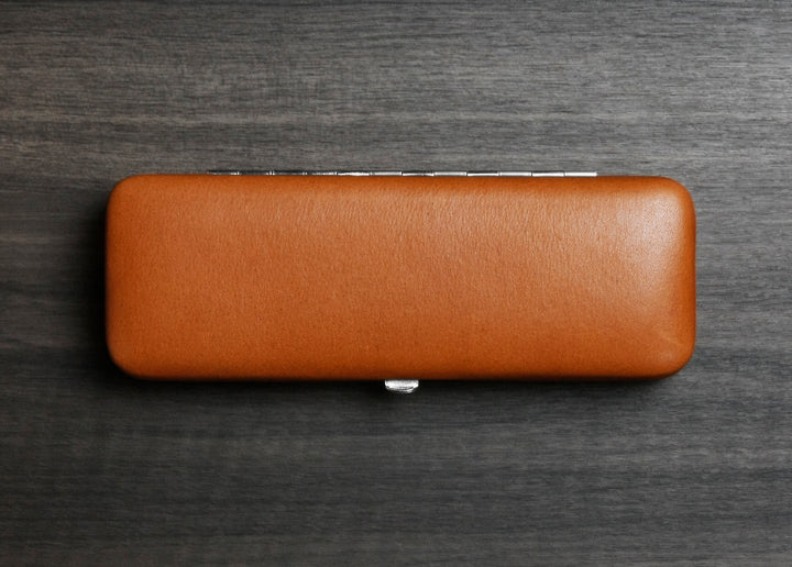 Top-down view of the F. Hammann 3883 Coxorange leather case, showcasing its flat, pocket-friendly footprint on a textured dark wood surface.