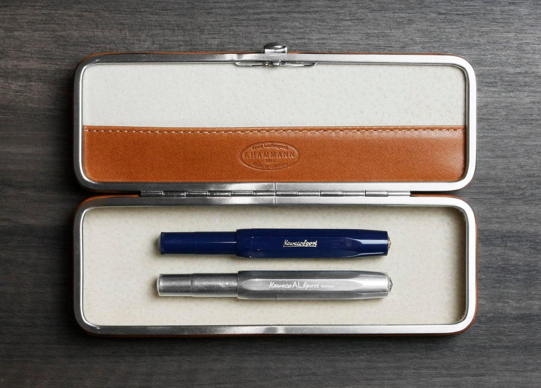 F. Hammann 3883 flexible framed case in Coxorange holding two pens securely under the adaptive, single-bridge system on a wood background.