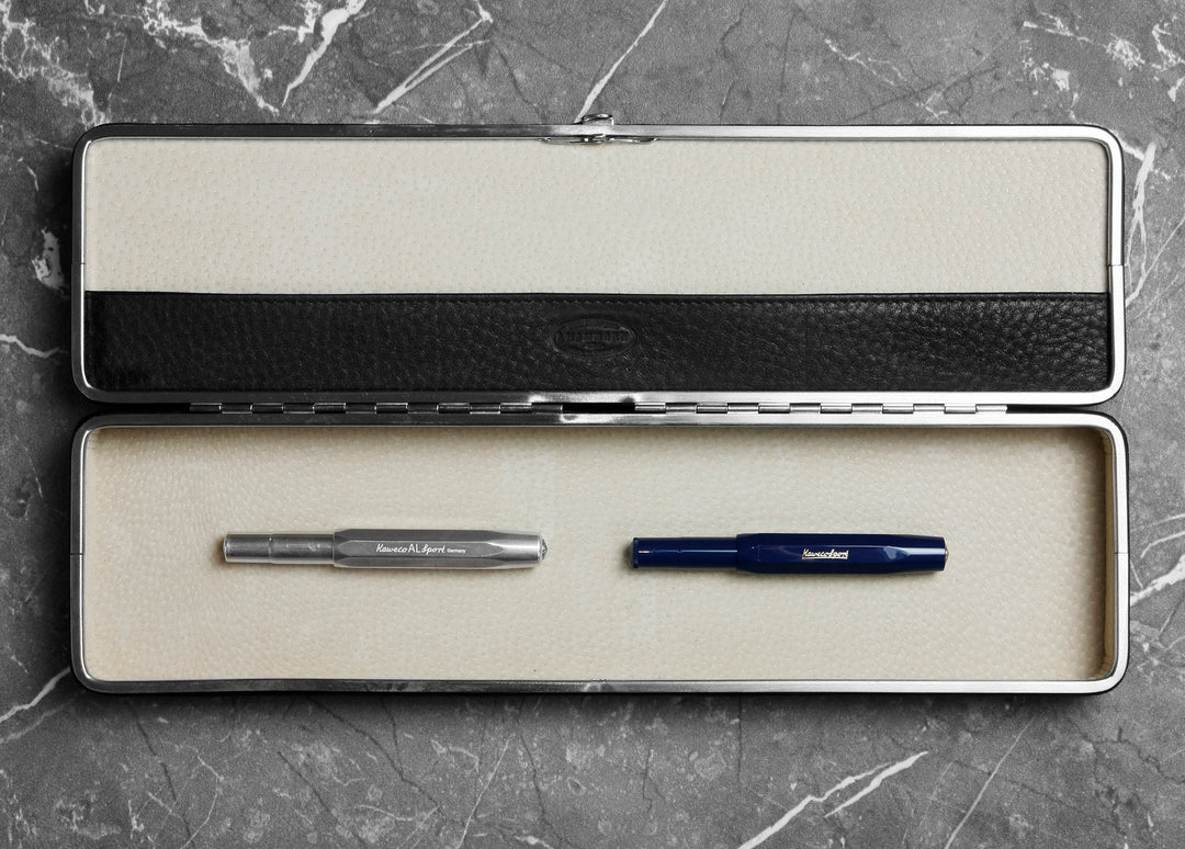 Open F. Hammann 3976 black leather case on marble, revealing a beige suede interior holding two Kaweco fountain pens.
