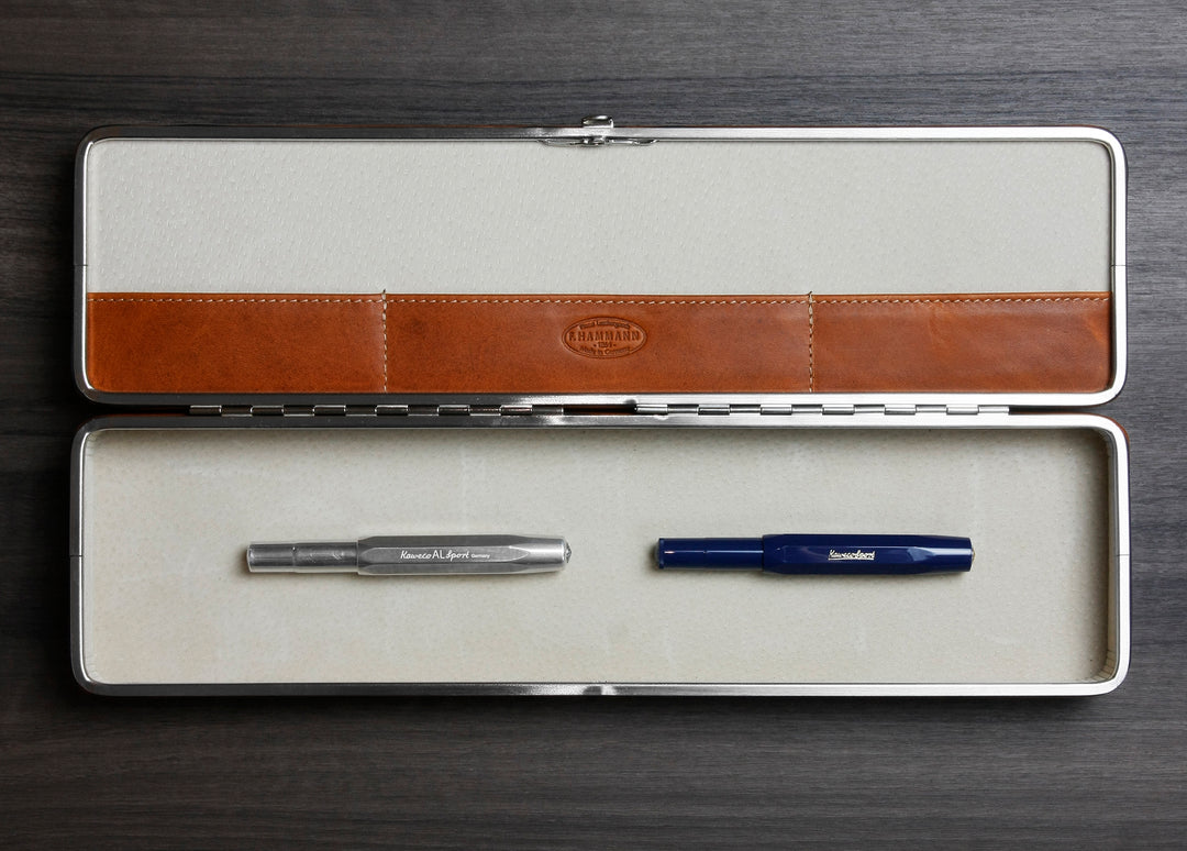 Open F. Hammann 3976 Ruler Box on dark wood, showing its beige suede interior and Coxorange leather holding two Kaweco pens.