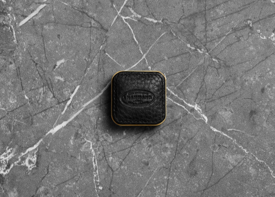 Top-down photograph of the F. Hammann 5205 Black Chervo Leather Tape Measure resting on grey marble.