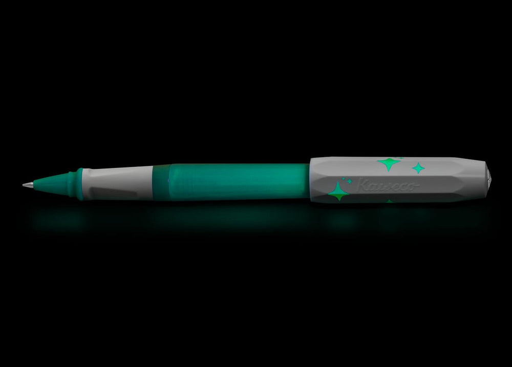 The Kaweco Perkeo Glow rollerball pen glowing vividly in a dark environment, demonstrating the luminescent green effect on the barrel, front grip section, and the printed star details on the cap.