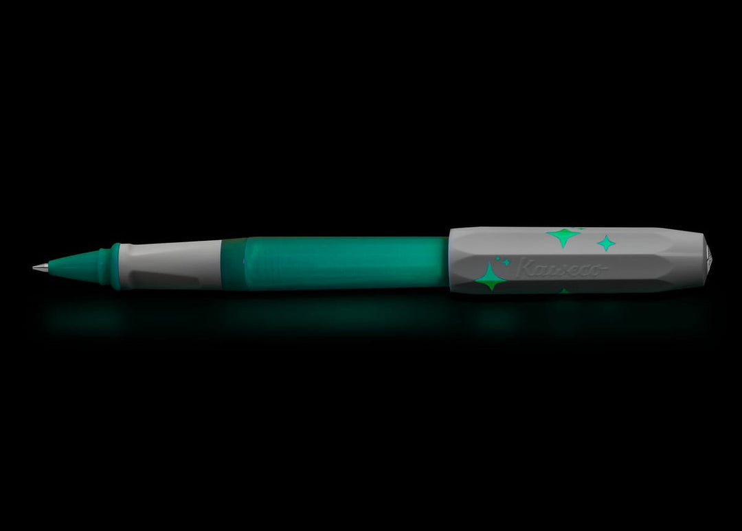 The Kaweco Perkeo Glow rollerball pen glowing vividly in a dark environment, demonstrating the luminescent green effect on the barrel, front grip section, and the printed star details on the cap.