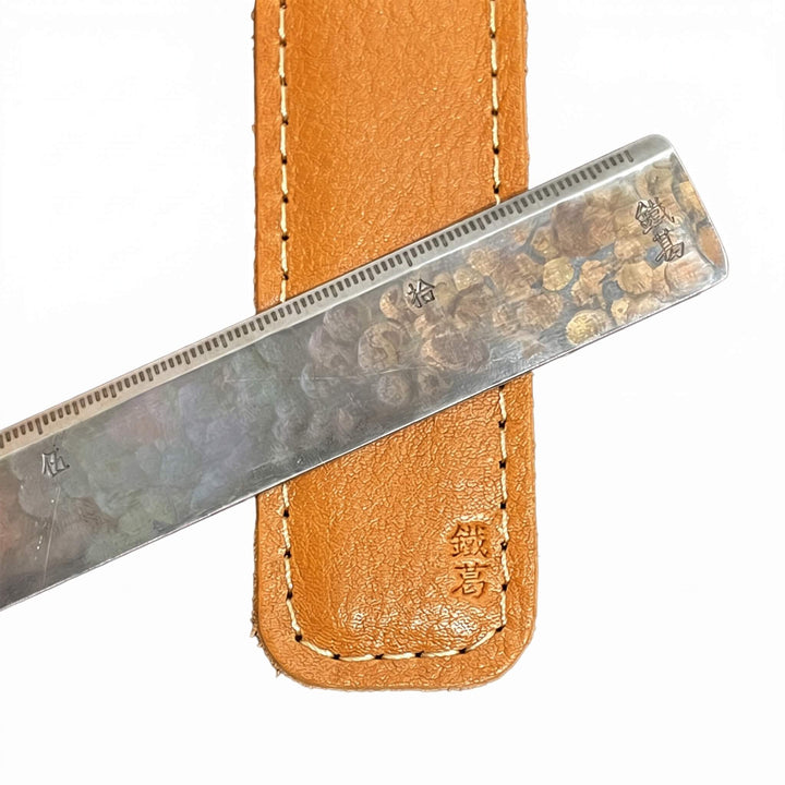 Close-up of a Japanese 3mm stainless steel straight ruler resting across its stitched tan leather sleeve.
