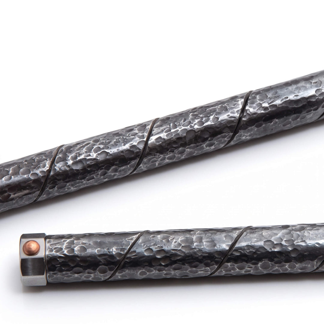 Macro shot of the Tsuchime hammered finish and spiral maki-hari seam on a dark steel pen barrel.