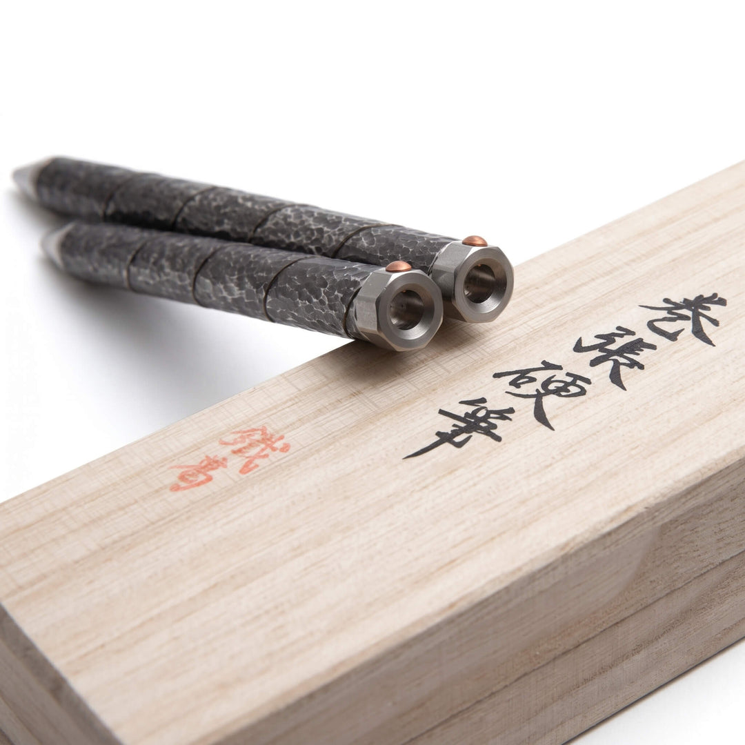 Two Kurogane Kazura Maki-hari hammered ballpoint pens resting on a branded Paulownia wood gift box.