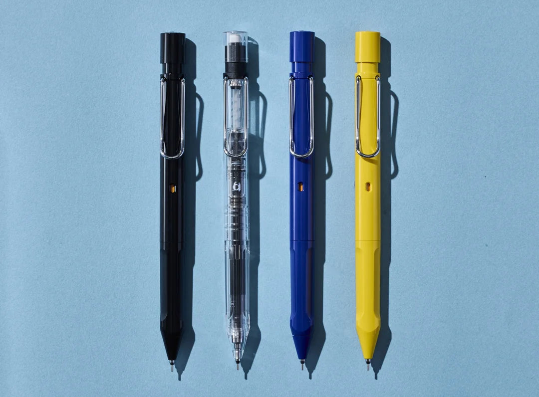 Top-down flat lay of four LAMY safari KURUTOGA mechanical pencils aligned perfectly on a light blue background, featuring the black, Vista Clear, blue, and yellow models.