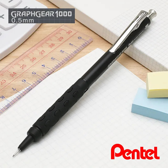 Stealth black Pentel GraphGear 1000 Anniversary Edition PG1015-ANA mechanical pencil on a desk alongside a drafting ruler and sticky notes.