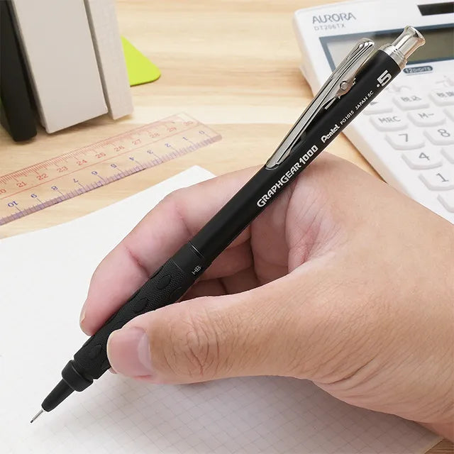 Hand holding the heavy-duty Pentel GraphGear 1000 Anniversary Edition PG1015-ANA 0.5mm stealth black pencil on grid paper.