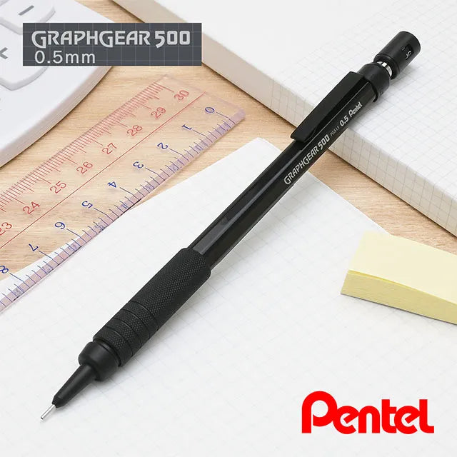 Pentel GraphGear 500 PG515 mechanical pencil in black, resting on a desk with a notebook, ruler, and keyboard, featuring the Pentel logo.