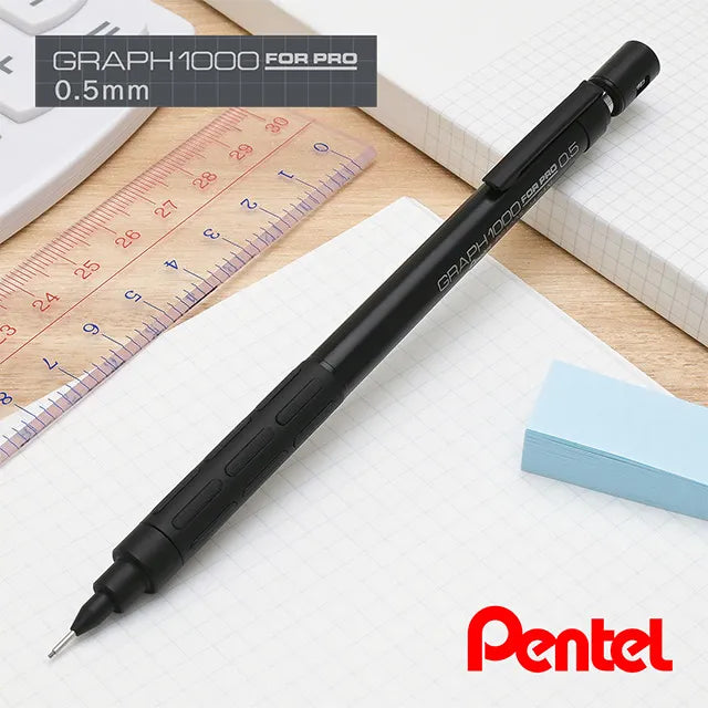 Stealth black Pentel Graph 1000 Anniversary Edition PG1005-ANA mechanical pencil on a desk alongside a drafting ruler and notebooks.