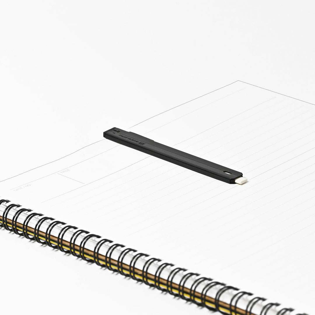 SEED Slendy Plus 2 Slim Holder Eraser in Black resting on an open spiral notebook, demonstrating its ultra-thin everyday carry profile.