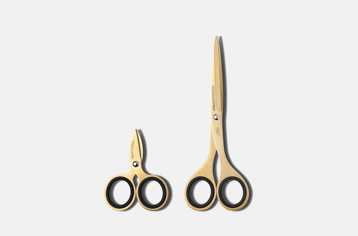 Size comparison of the TOOLS to LIVEBY gold scissors collection, featuring the ultra-compact 3-inch micro-EDC pocket model alongside the full-sized studio shears, both resting vertically on a minimalist white surface.