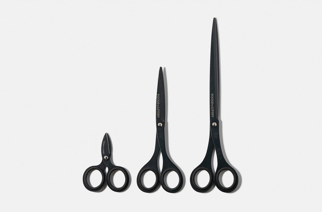 Size comparison of the TOOLS to LIVEBY matte black scissors collection, featuring the ultra-compact 3-inch micro-EDC model alongside the 6.5-inch pouch scissors and the full-sized studio shears standing vertically on a white surface.