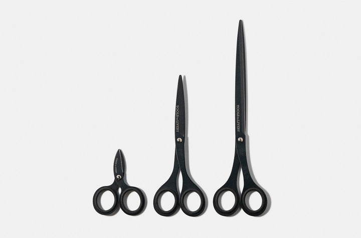 Size comparison of the TOOLS to LIVEBY matte black scissors collection, featuring the ultra-compact 3-inch micro-EDC model alongside the 6.5-inch pouch scissors and the full-sized studio shears standing vertically on a white surface.