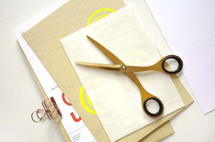 Premium overhead flat lay featuring the TOOLS to LIVEBY 6.5-inch gold scissors resting open on textured stationery and kraft paper, highlighting its precision design for papercraft and journaling.