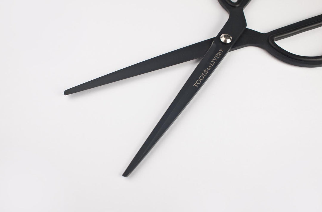 Macro close-up of the open TOOLS to LIVEBY matte black scissors, showcasing the sharp inner edge of the Japanese stainless steel blades and the precise anti-adhesive Teflon coating.