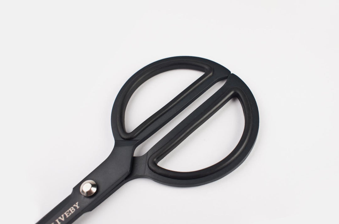 Macro detail of the TOOLS to LIVEBY matte black scissors' handle, highlighting the ergonomic, heavy-duty metal loops and the tactical, ultra-matte Teflon finish.