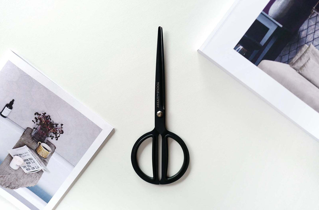 Premium flat lay aesthetic featuring the TOOLS to LIVEBY 8-inch matte black scissors placed vertically on a white studio desk alongside modern art, lifestyle, and design magazines.
