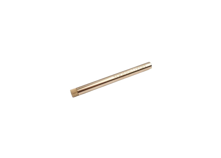 Fully closed TOOLS to LIVEBY raw brass lead holder resting diagonally on a white surface, highlighting the minimalist pocket-sized everyday carry design and engraved brand logo.
