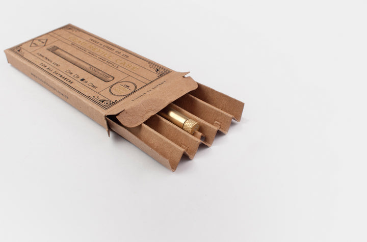 TOOLS to LIVEBY raw brass lead holder partially slid out of its vintage foil-stamped cardboard matchbox packaging on a minimalist white surface.