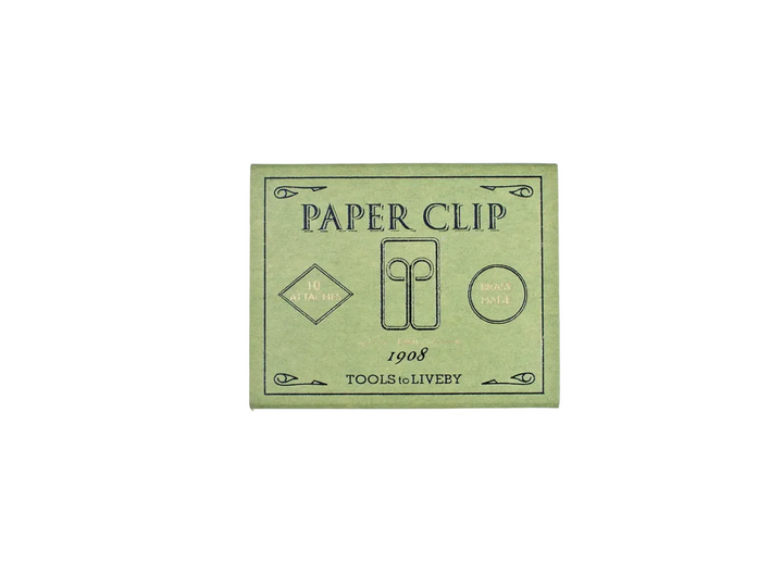 A direct top-down product shot of the closed, emerald green sliding matchbox for the TOOLS to LIVEBY Owl brass paper clip, showcasing the elegant black typography and gold foil-stamped accents detailing its 1908 heritage.