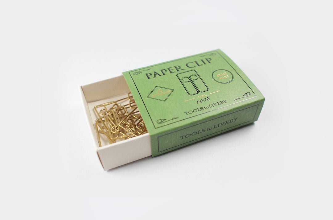 An open vintage-style emerald green sliding matchbox revealing a tangled cluster of gleaming raw brass Owl paper clips resting in the tray against a clean white background.