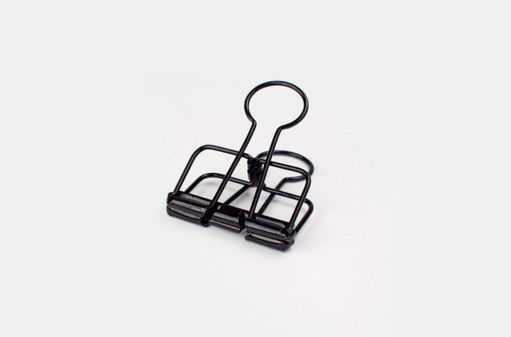 A detailed front-facing close-up shot of a single TOOLS to LIVEBY matte black skeleton binder clip standing on its base against a plain white background, displaying its full wireframe structure.