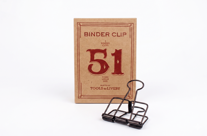 A large 51mm TOOLS to LIVEBY Skeleton Binder Clip in bronze resting in front of its matching vintage foil-stamped kraft paper box.
