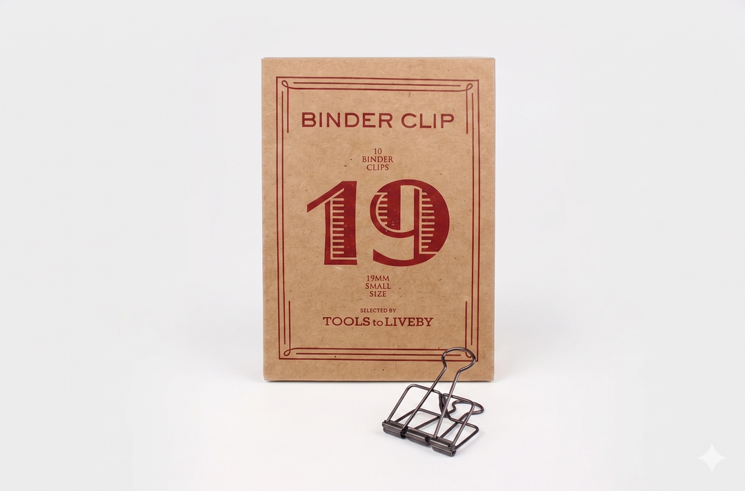 A small 19mm TOOLS to LIVEBY Skeleton Binder Clip in bronze displayed alongside its iconic foil-stamped kraft paper unboxing package.