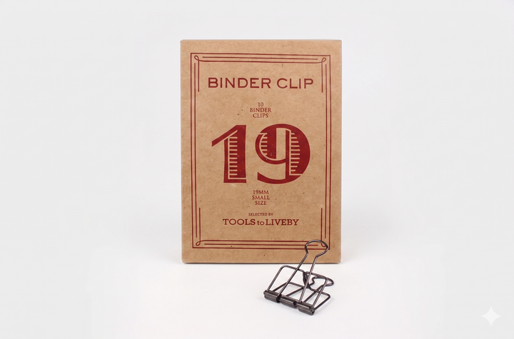 A small 19mm TOOLS to LIVEBY Skeleton Binder Clip in bronze displayed alongside its iconic foil-stamped kraft paper unboxing package.