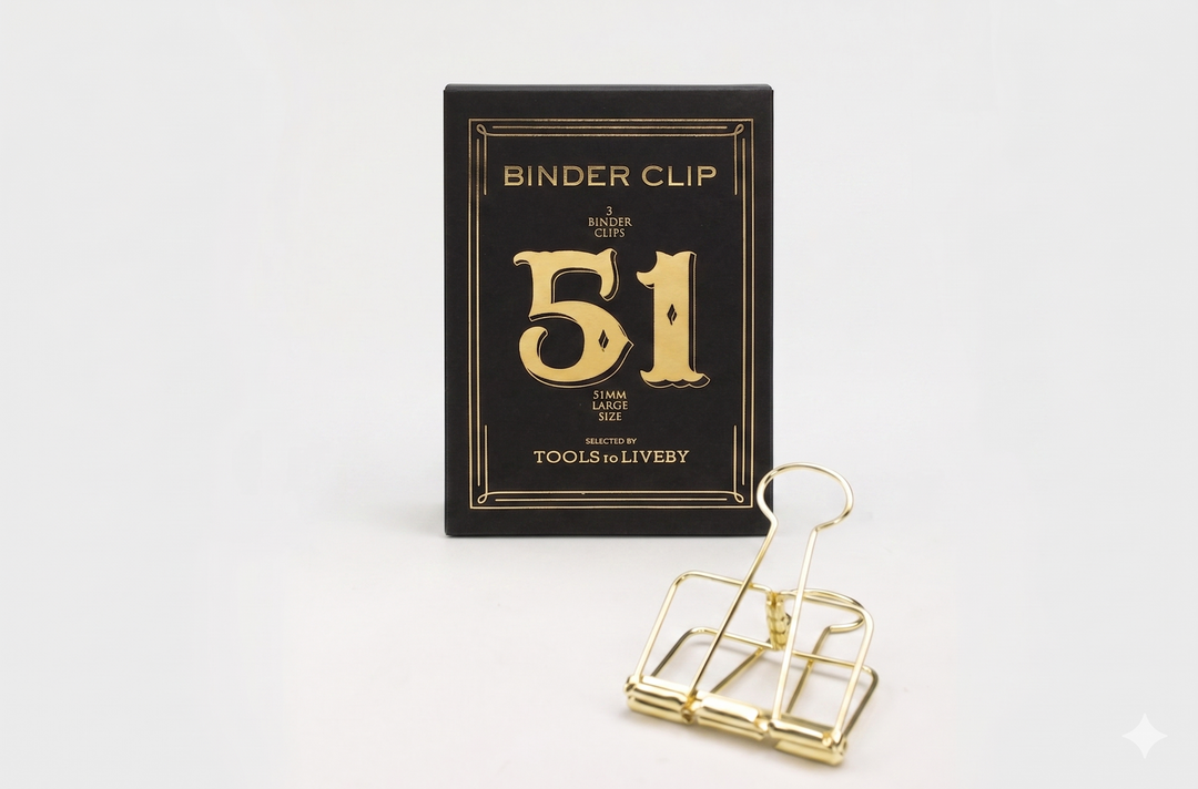 A large 51mm TOOLS to LIVEBY gold skeleton binder clip resting in front of its premium black packaging, which features a prominent gold foil-stamped number 51.