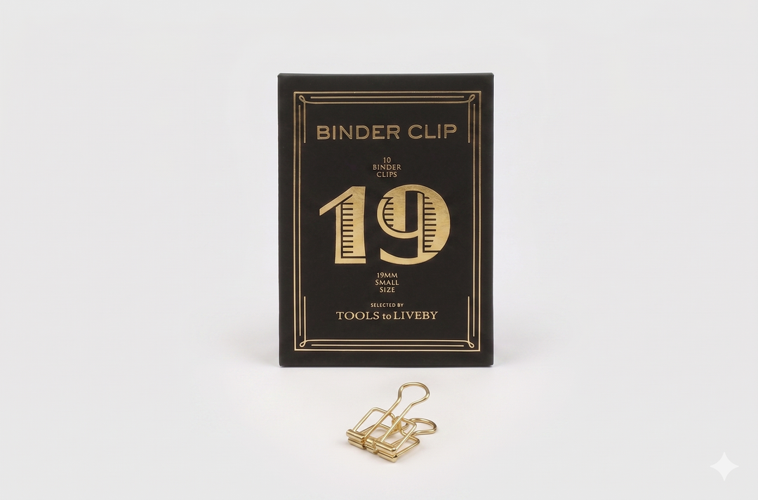 A small 19mm TOOLS to LIVEBY gold skeleton binder clip positioned neatly in front of its black product box, showcasing a distinct striped gold foil-stamped number 19.