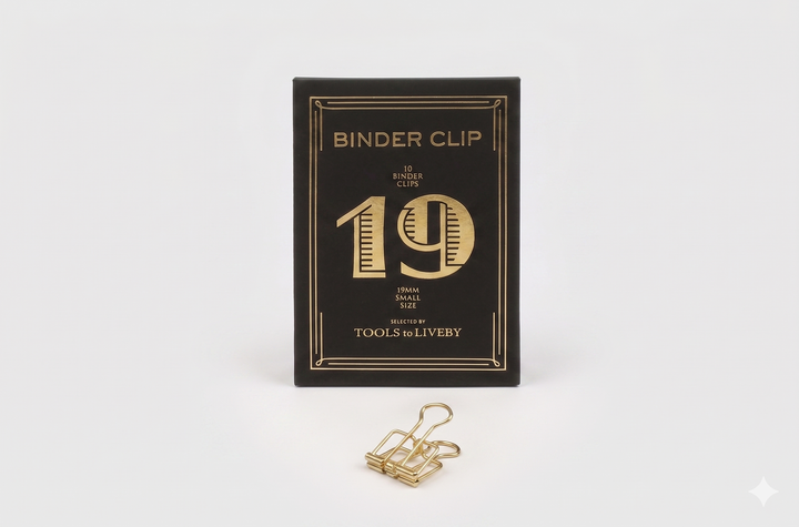 A small 19mm TOOLS to LIVEBY gold skeleton binder clip positioned neatly in front of its black product box, showcasing a distinct striped gold foil-stamped number 19.