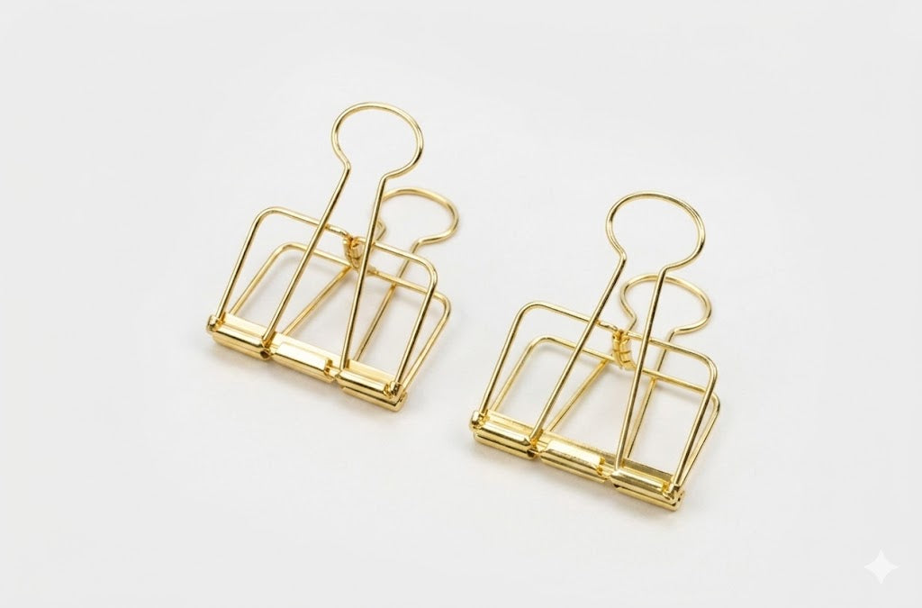 Two gold TOOLS to LIVEBY skeleton binder clips standing upright on their bases against a clean white background, showcasing the hollow see-through wire silhouette.