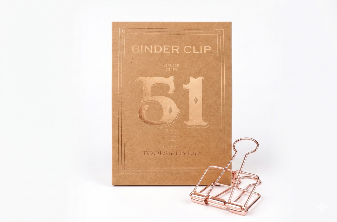 A large 51mm TOOLS to LIVEBY Skeleton Binder Clip in a luxurious Rose Gold finish, displayed alongside its sophisticated, vintage-inspired foil-stamped kraft paper box which prominently features the number '51'.