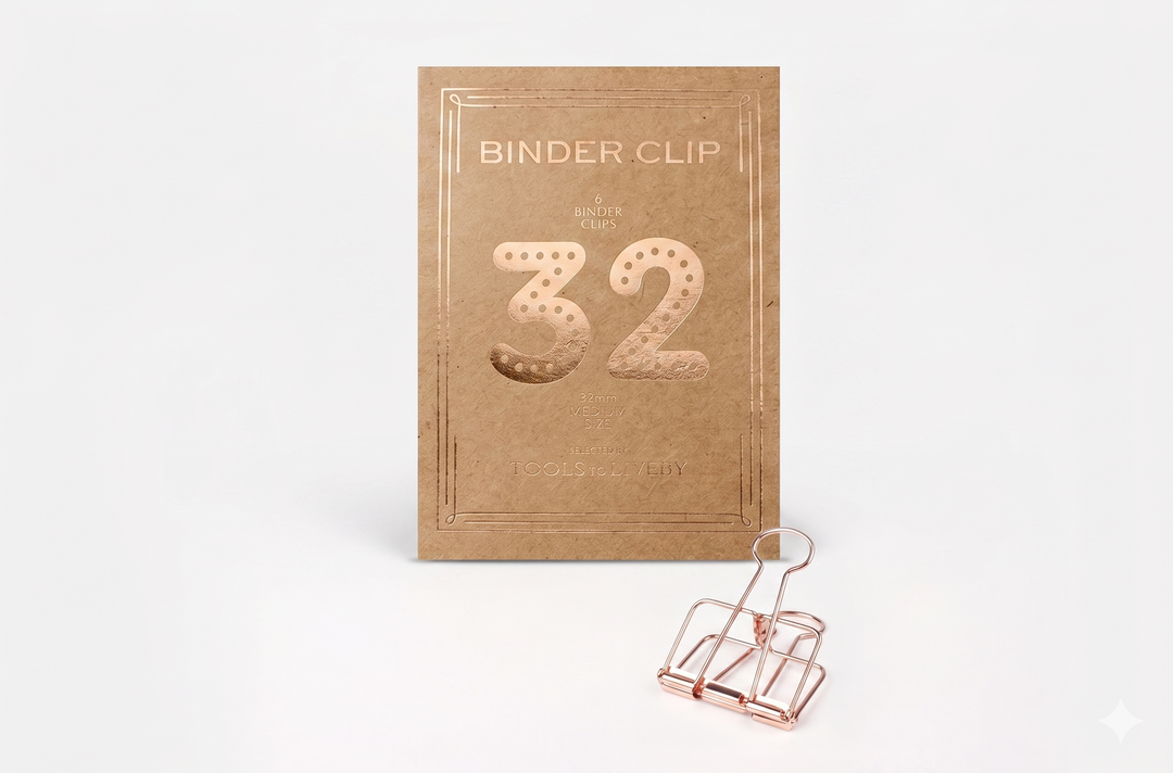 A medium 32mm TOOLS to LIVEBY Skeleton Binder Clip in elegant Rose Gold, standing before its premium kraft packaging that showcases a stylish foil-stamped '32' and brand typography.