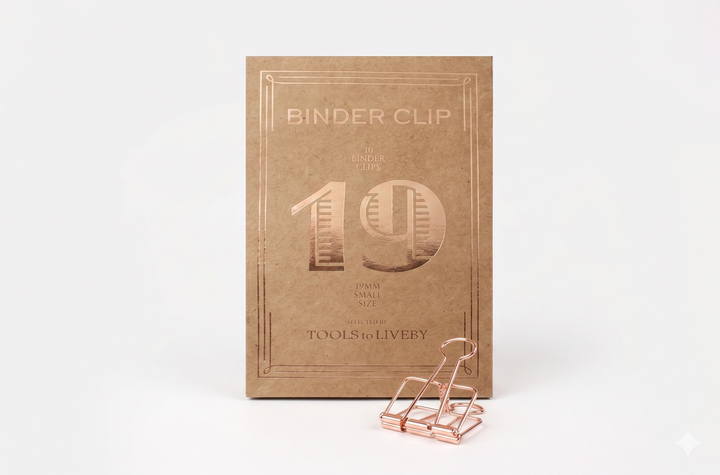 A small 19mm TOOLS to LIVEBY Skeleton Binder Clip in delicate Rose Gold, resting on a clean white surface next to its signature vintage-style kraft paper box marked with the number '19'.