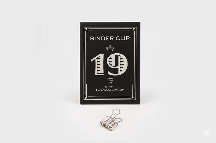 A small 19mm TOOLS to LIVEBY silver skeleton binder clip positioned neatly in front of its black product box, showcasing a distinct striped silver foil-stamped number 19.