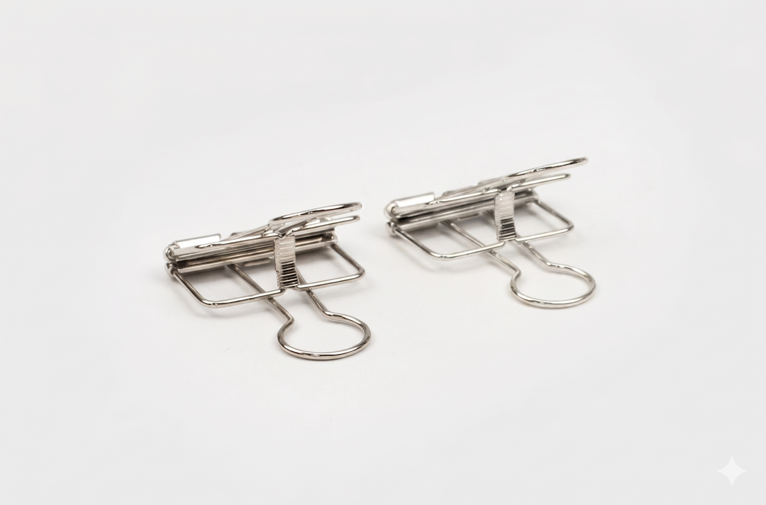 A close-up side angle of two silver TOOLS to LIVEBY skeleton binder clips resting on a white background, highlighting the high-polish chrome finish and architectural tension mechanism.