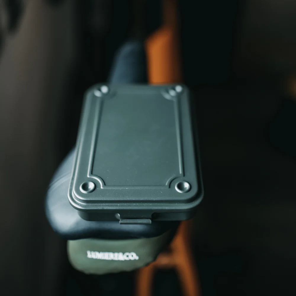 Closed Moss Green TOYO T-152 Steel Toolbox resting on a bicycle saddle, highlighting its portable, flat EDC profile.